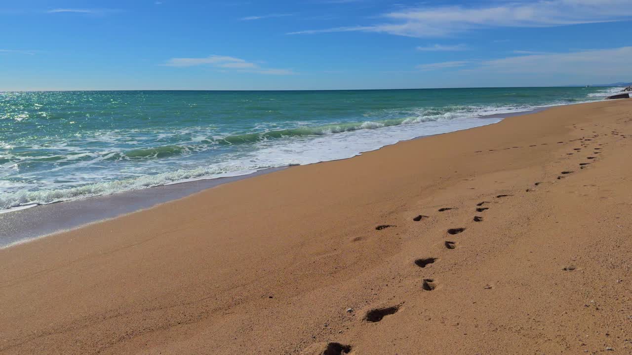 Passeggiata su una spiaggia deserta, impronte nella sabbia in primo piano, movimento fluido con il mare sullo sfondo.