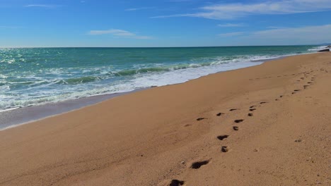 walking on the beach without people, footprints in the sand in the foreground, smooth movement with the sea in the background