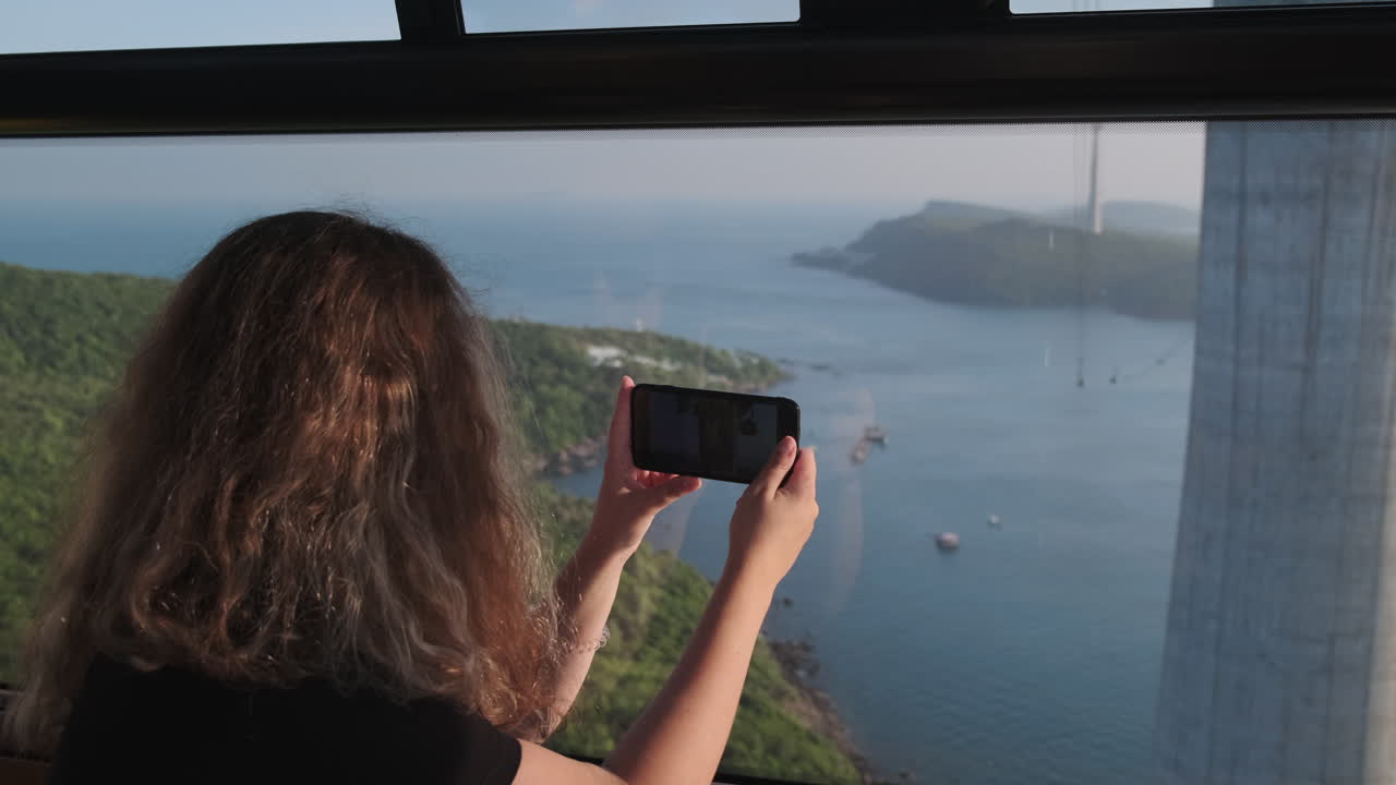 mujer tomando una foto de una hermosa vista del océano desde un teleférico