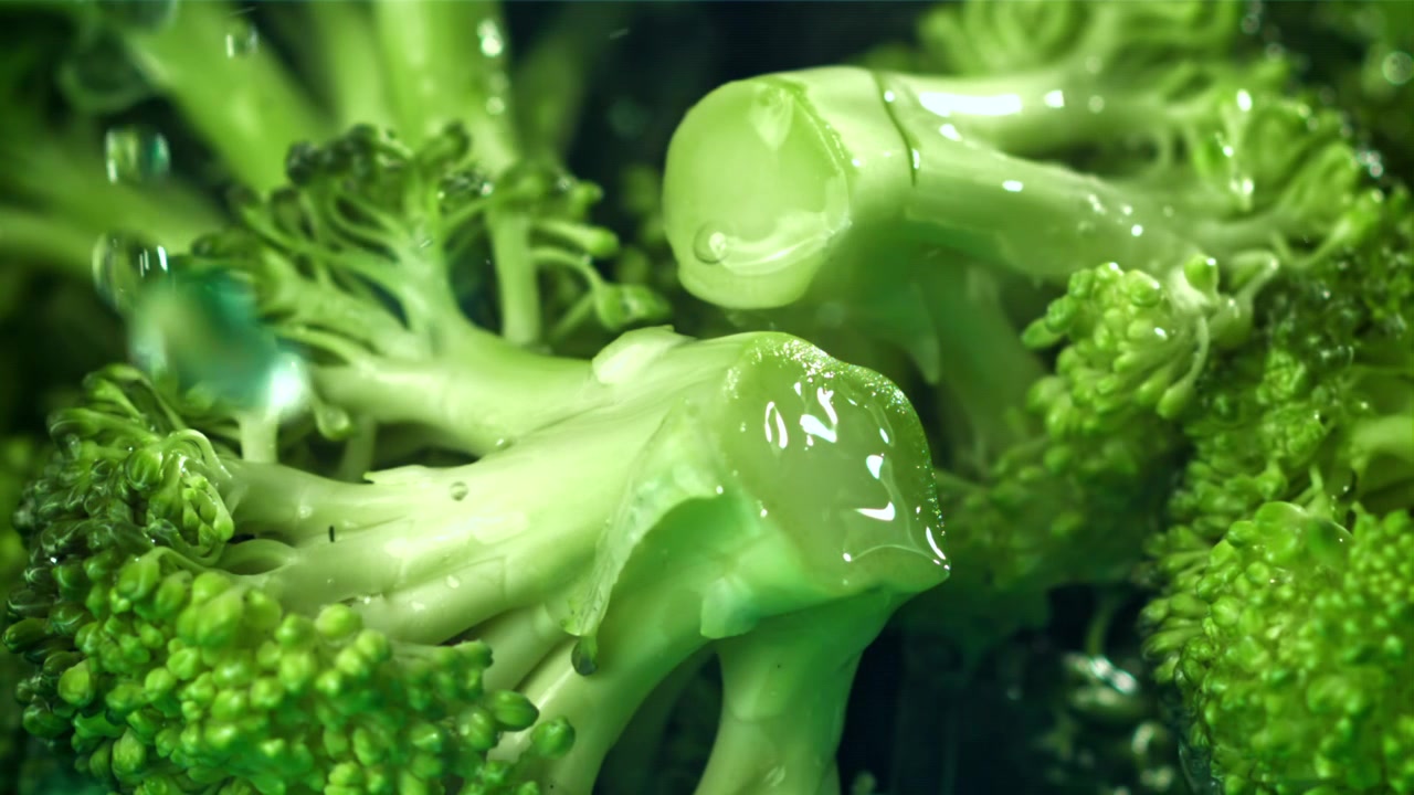 Gocce d'acqua che schizzano su cimette fresche di broccoli verdi