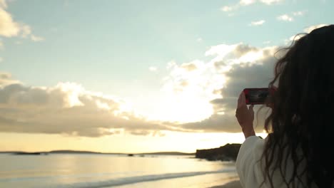 mujer morena tomando una foto de la puesta de sol en su teléfono inteligente