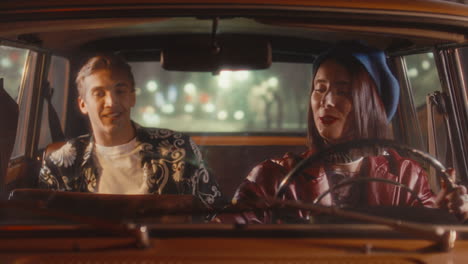 young couple driving retro car at night, smiling and having talk