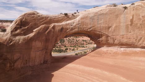 aerial backward of man walking over wilson arch rock formation, utah