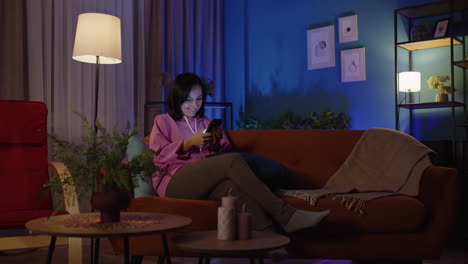 Woman-texting-message-on-smartphone,-scrolling-on-mobile-phone-and-lying-on-sofa-at-home-alone