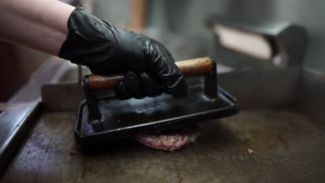 Preparing-a-beef-burger-patty-on-a-stove-with-black-gloves