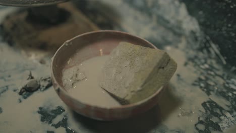wet sponge in clay bowl resting on messy pottery table during ceramic process