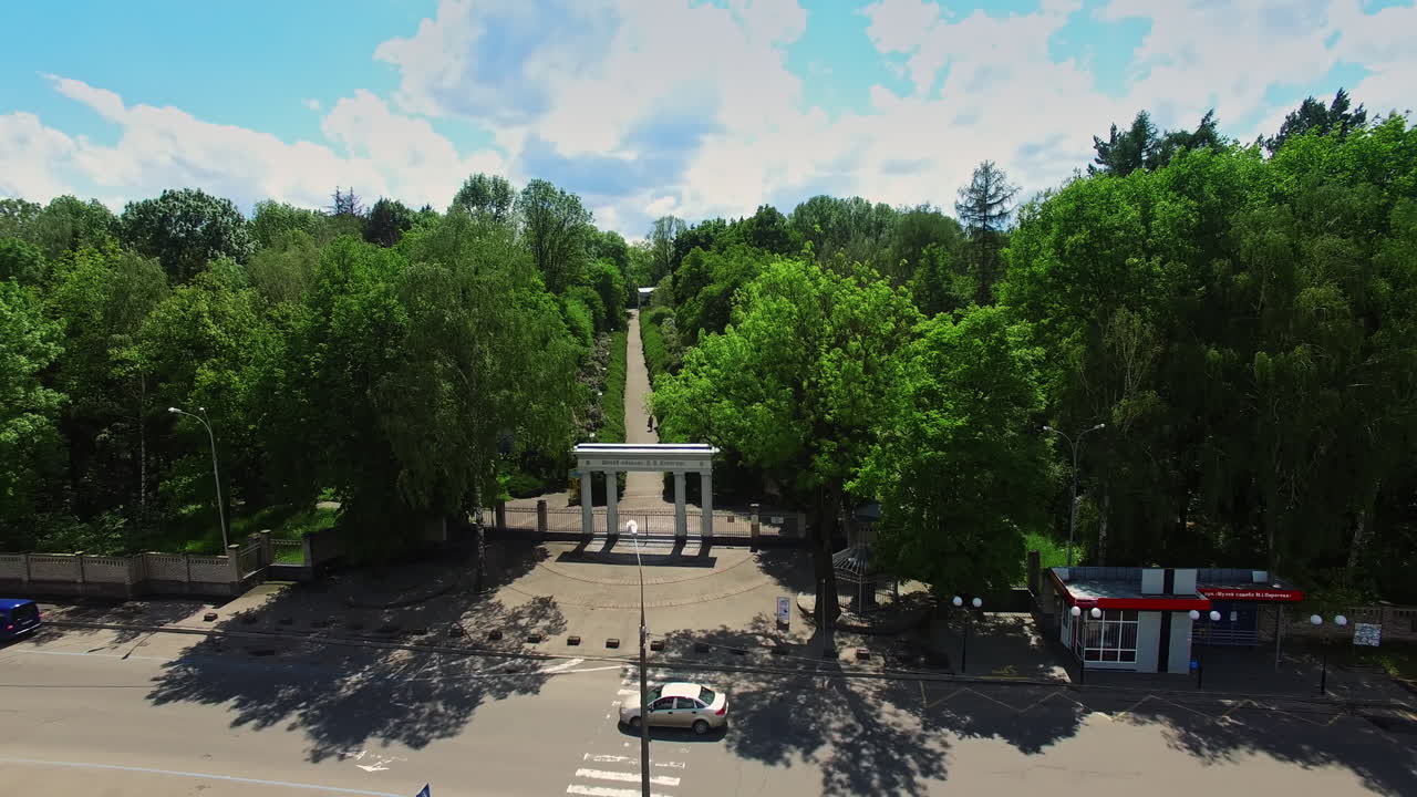 White columns at the entrance to the beautiful green park. Drone footage over the car road and lawn. Sunny day backdrop.