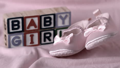 baby booties falling on pink blanket with baby girl message in blocks