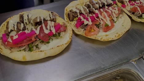 zoom de primer plano en pita wrap kebab shish shawarma sándwiches de carne de cordero que se preparan en la cocina de un lugar de comida rápida y salsa de ajo tahini que se rocía en el mostrador de acero inoxidable