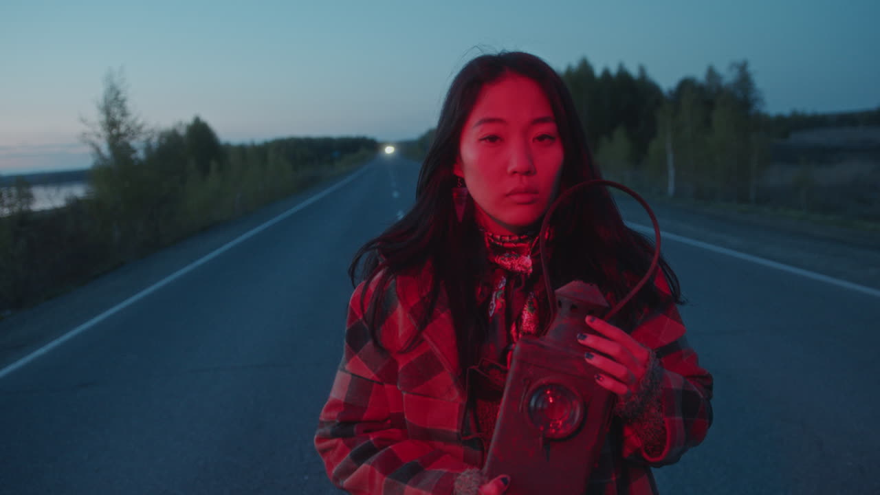 retrato de una mujer asiática con una linterna brillante en una carretera vacía al anochecer