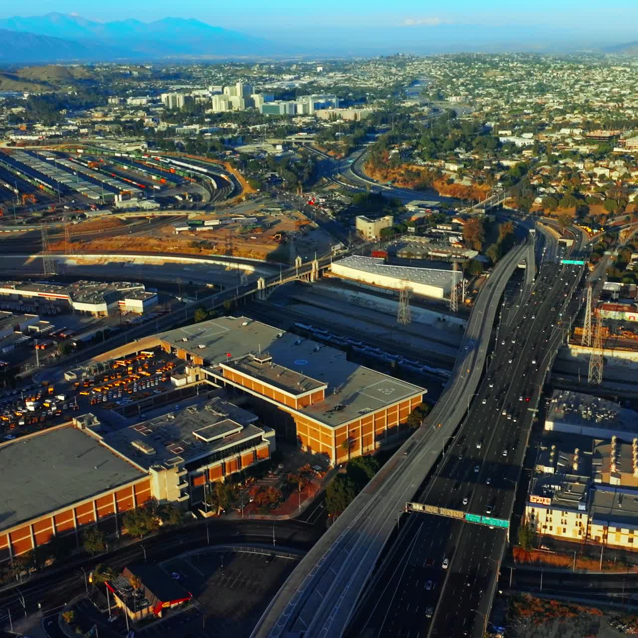 Lively traffic on the highways of Los Angeles at daytime. Sunny panorama of the city at backdrop of mountains. Top view
