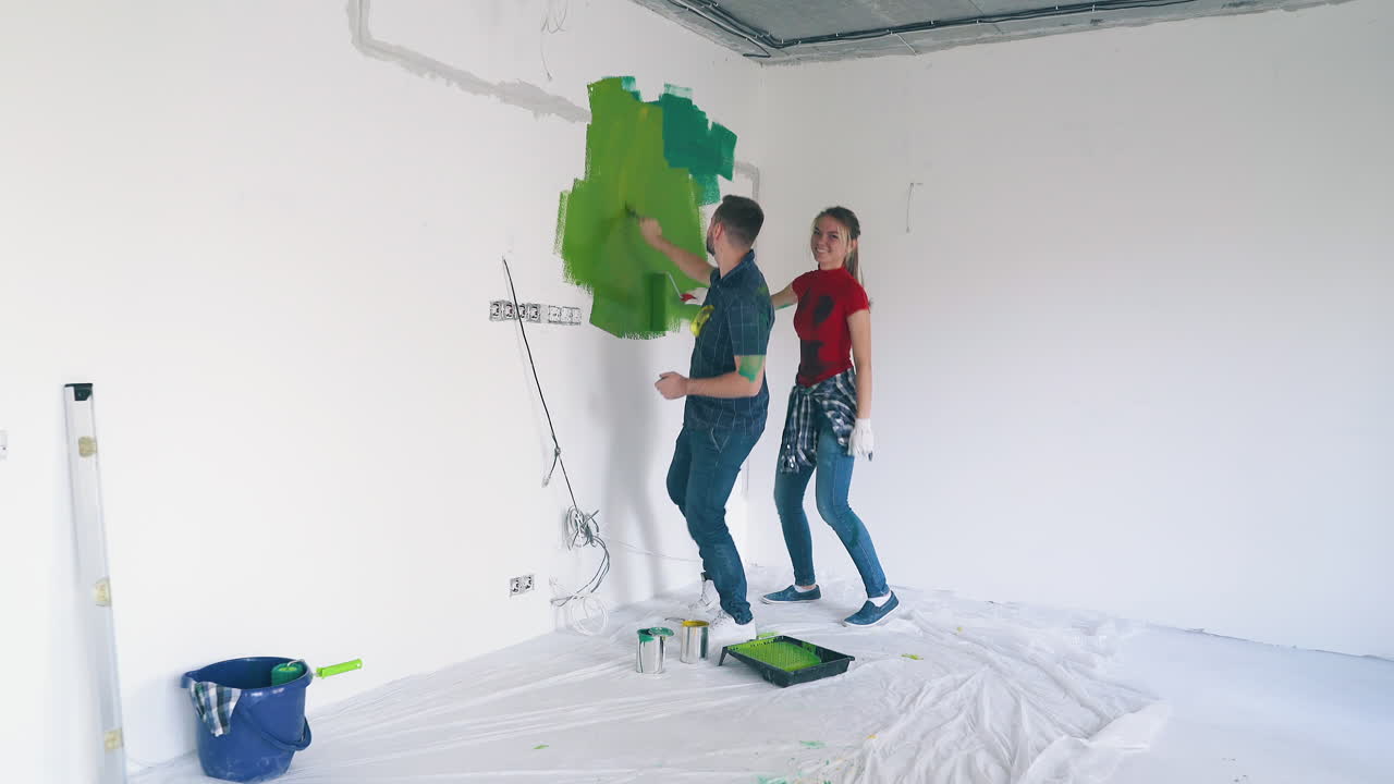 familia de chico y chica baila pintando pared blanca en la habitación