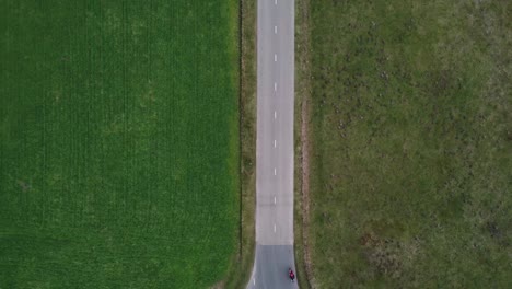 aerial shot of motorcyclist driving down a straight road between fields