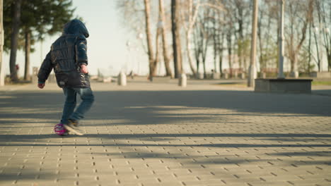 close up of a child is seen playfully chasing a balloon along a paved path near a building, the child is dressed in a shiny black jacket, running towards the balloon as it floats along the ground