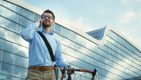 Good-looking-man-speaking-on-the-mobile-telephone-while-standing-with-his-bike-in-the-business-center-of-the-city