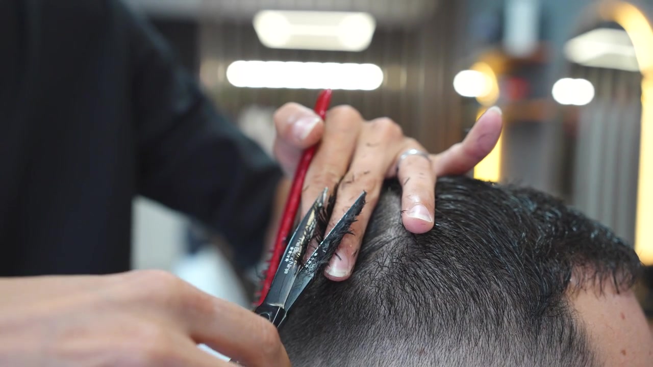 Parrucchiere professionista che usa pettine e forbici per tagliare i capelli a un uomo in una moderna barberia.