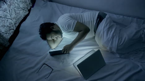 excited indian young man chatting with his girlfriend in his smartphone while lying on bed during night time