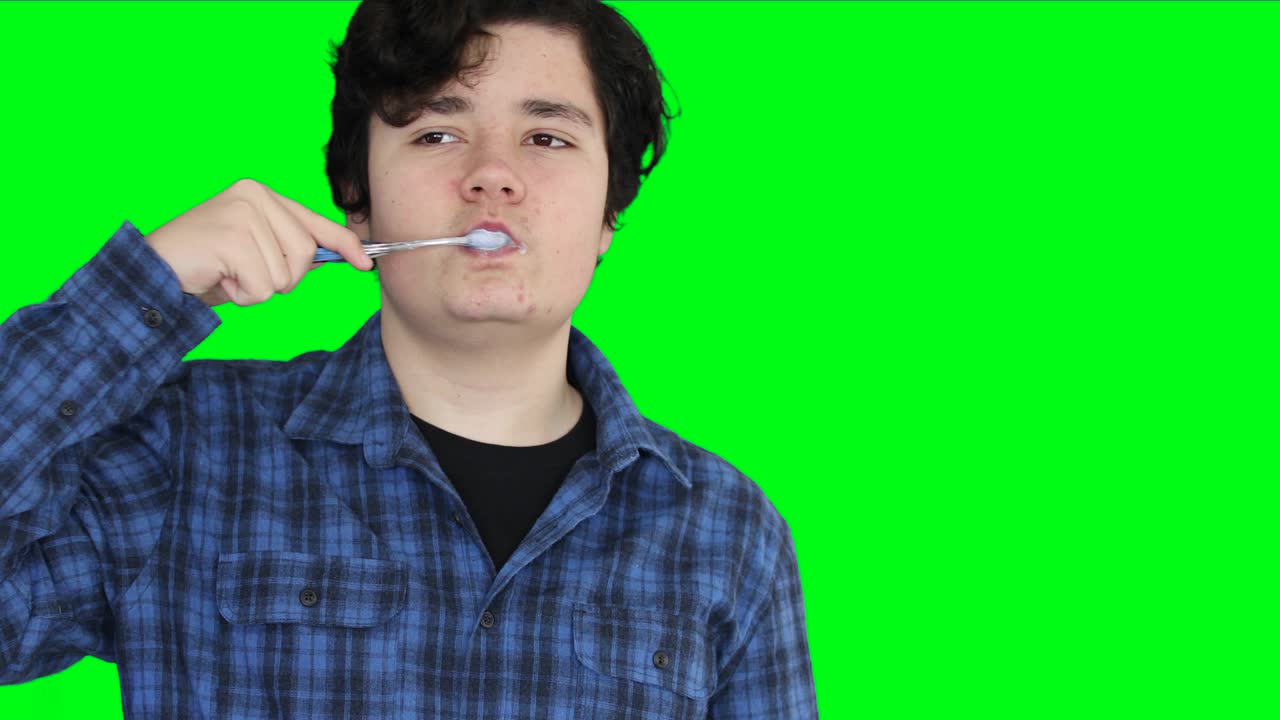 Teenage boy brushing his teeth at green screen background 2