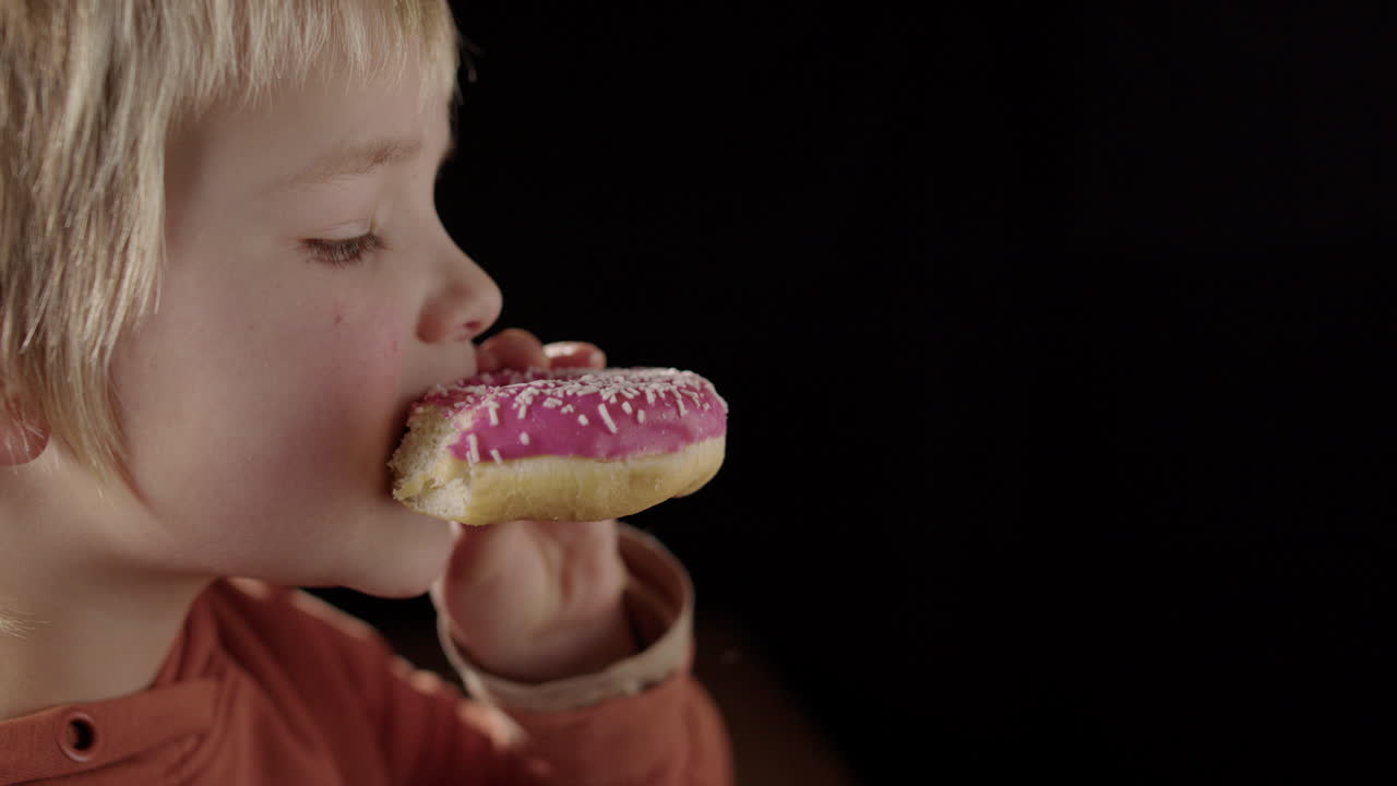 Tight profile view of caucasian boy biting into moist glazed doughnut