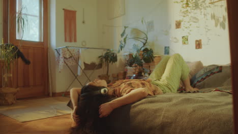 young woman relaxing on bed in sunlit room, listening to music with headphones