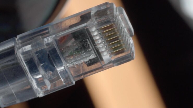 Transparent Ethernet connector showing gold contacts and internal wiring detail. Closeup view highlights clear plastic housing and network cable connection technology.