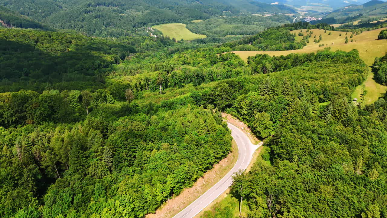 Picturesque rocky landscape covered with the green woods. Drone flight over the wavy highway crossing the scenery.