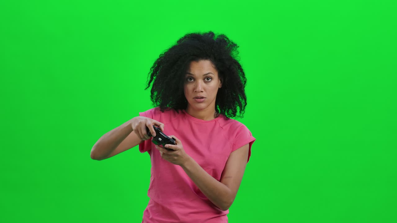 Portrait of young female African American playing a video game using a wireless controller. Black woman with curly hair poses on green screen in the studio. Close up. Slow motion ready 59.97fps