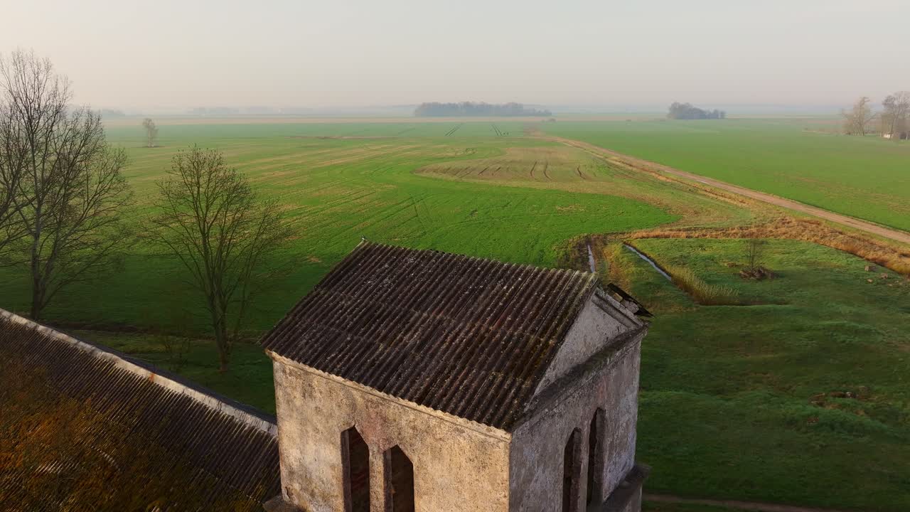 Aerial shot shows abandoned rural church at sunrise surrounded by green fields