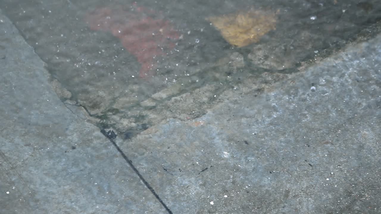 Raindrops falling on city pavement. Wet street with water reflections and splashes. Ideal for weather, mood, cinematic B-roll