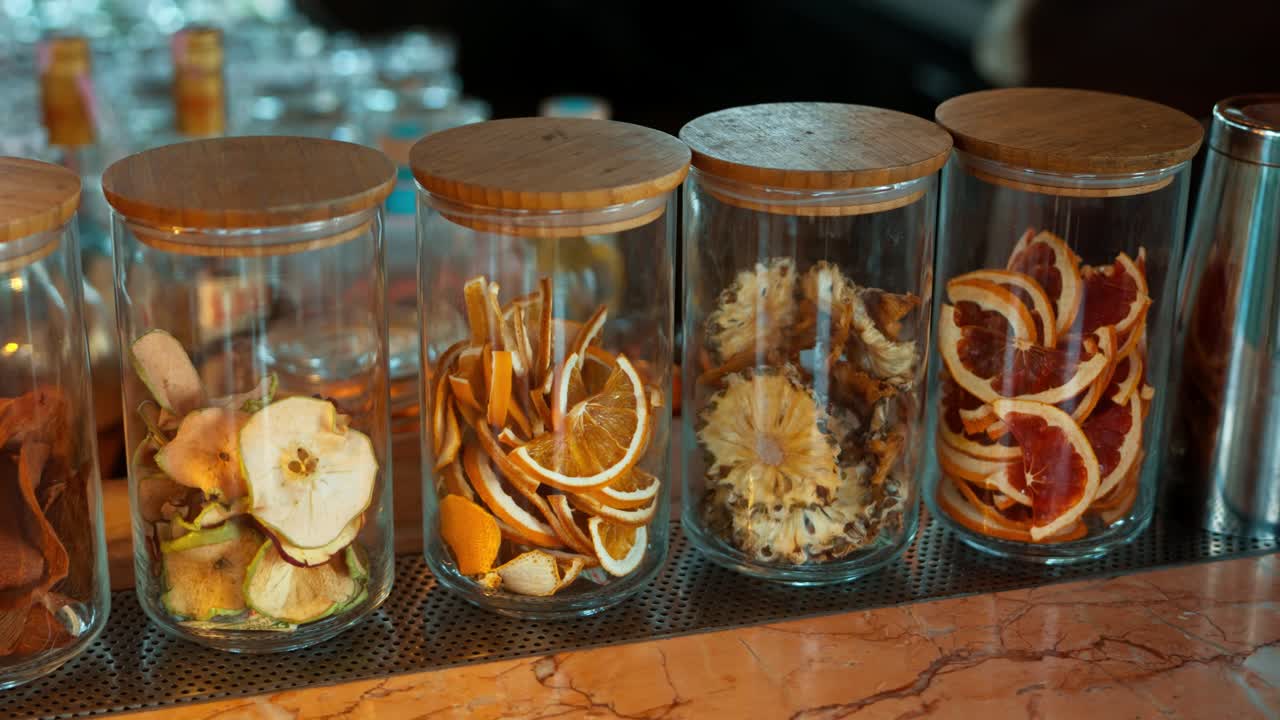 Glass jars filled with dried apple orange pineapple and citrus slices displayed at tropical beach cocktail bar - slow motion parallax
