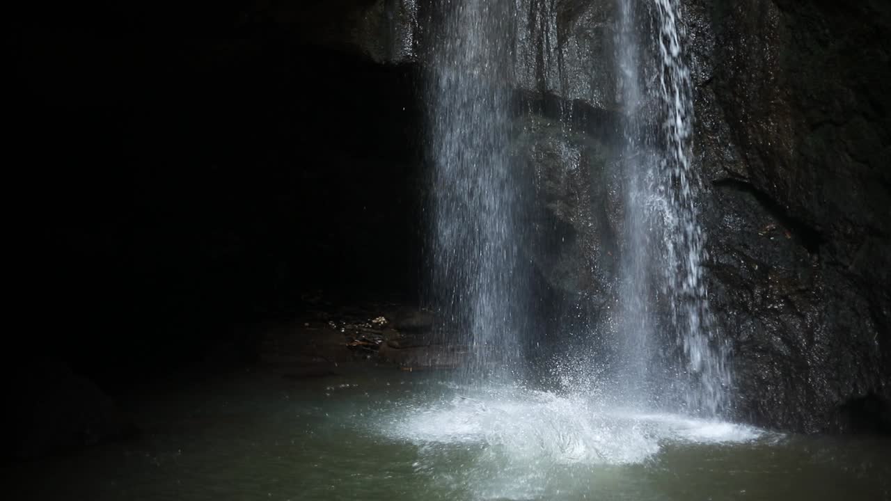 toma en cámara lenta de un hombre haciendo una voltereta hacia atrás desde un acantilado y frente a una cascada de leke leke en bali, indonesia, después de una tormenta de lluvia