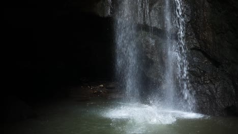 slow motion shot of a man doing a back flip off of a cliff and in front of a gushing leke leke waterfall in bali, indonesia following a rain storm