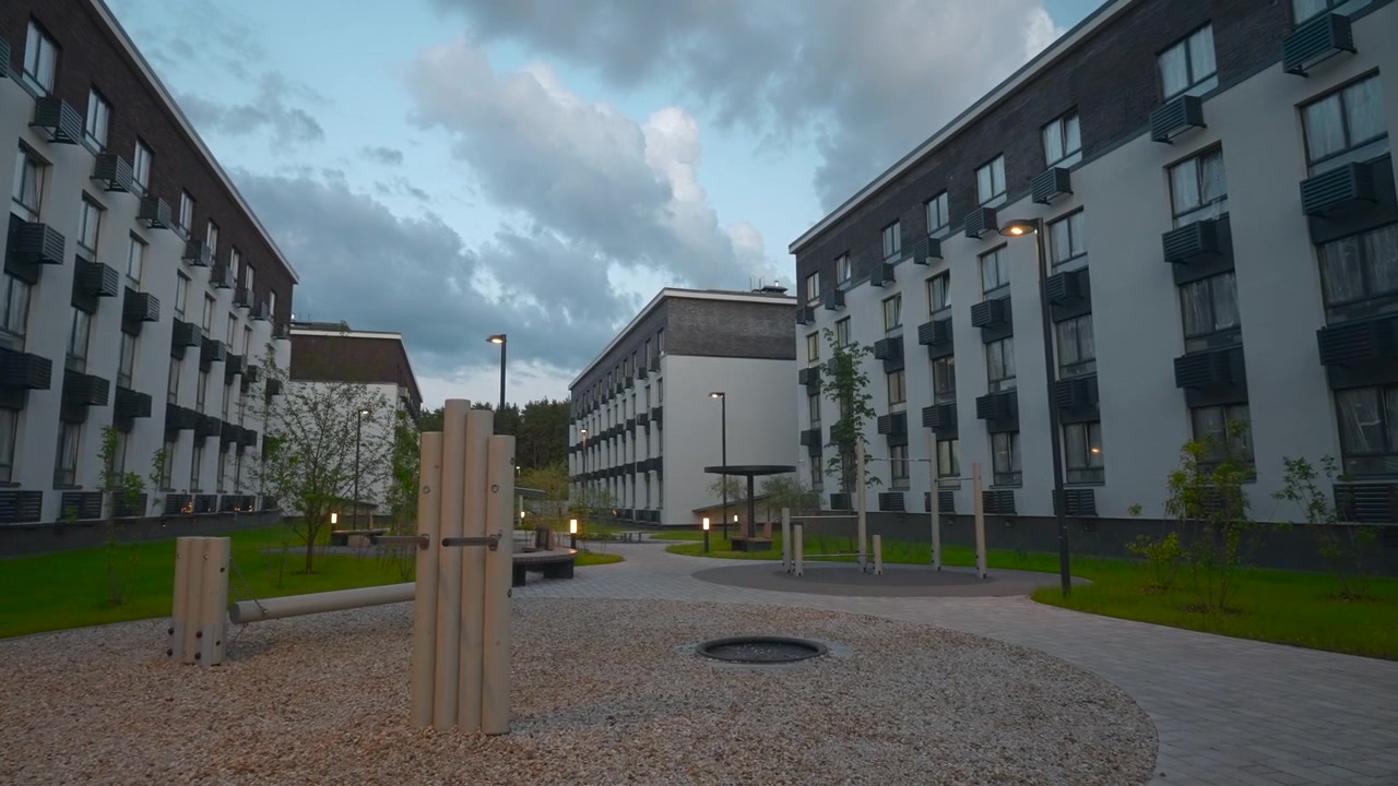 Verso la fine della sequenza, un tranquillo cortile residenziale rimane vuoto e immobile tra edifici residenziali simmetrici. L'area aperta principale si trova nel