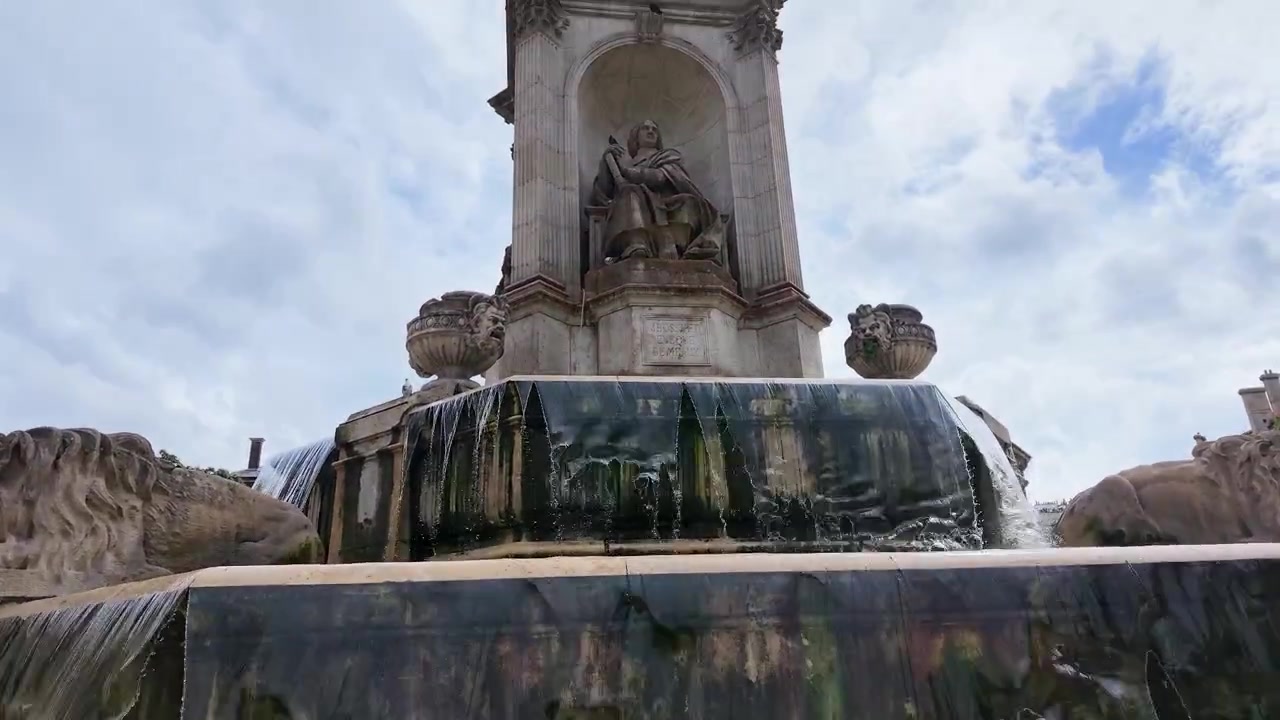 Una toma inclinada en ángulo bajo revela la ornamentada fuente de piedra y las estatuas bajo cielos nublados