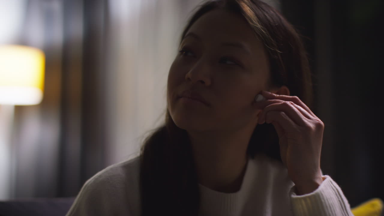 소파에서 집에서 저녁을 보내고 무선 이어을 착용하고 휴대전화에서 음악이나 캐스트를 스트리밍하는 여성의 클로즈업