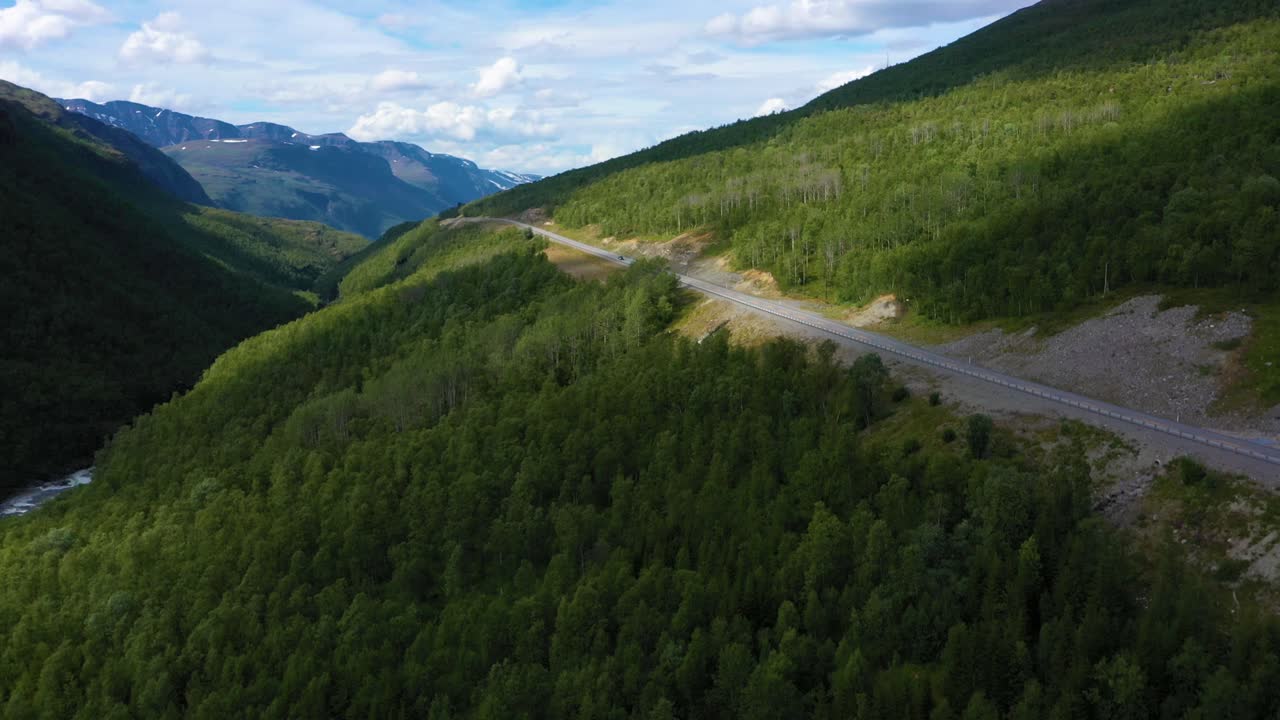 Aerial view of a asphalt, mountain road, Arctic fells in the background, sunny day, in Nordland, North Norway - rising, drone shot