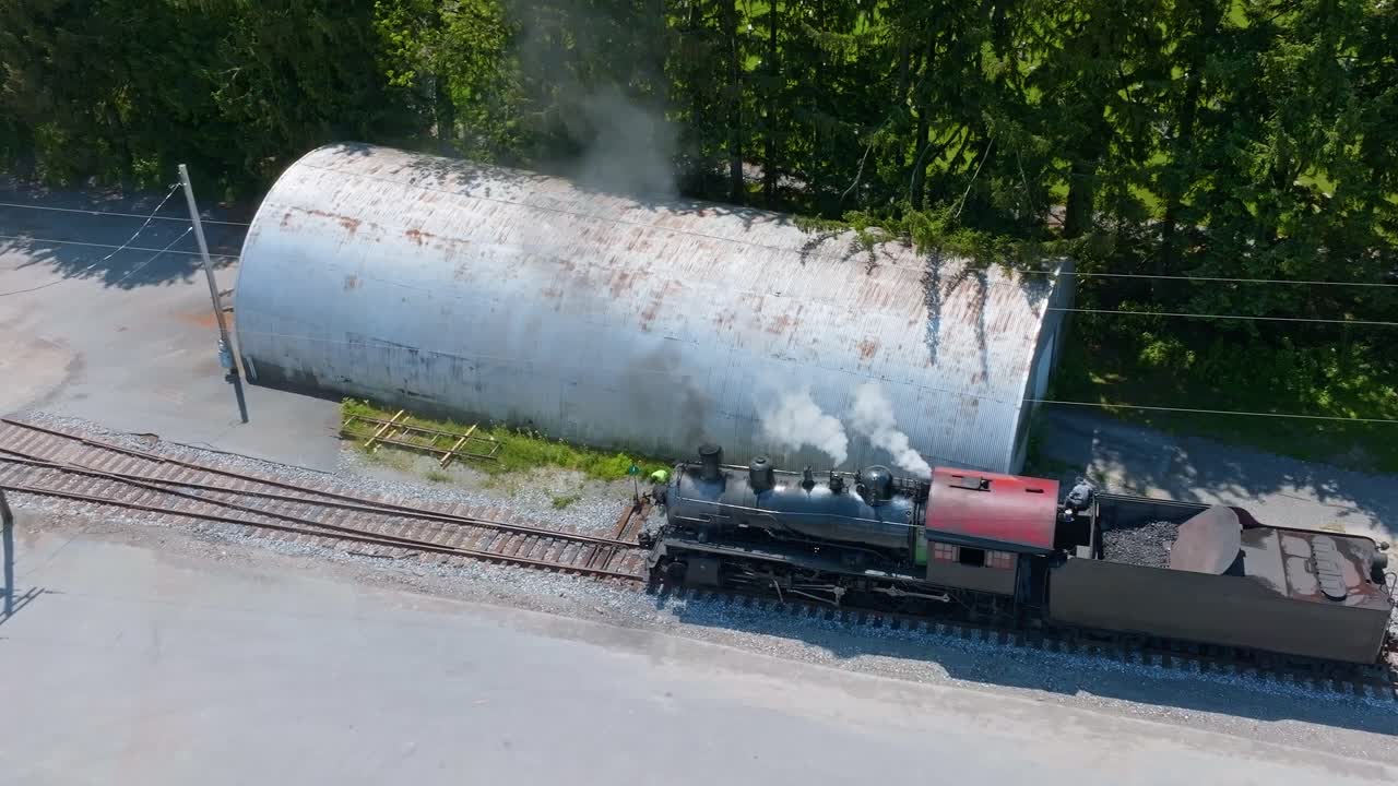 An aerial view of a vintage steam locomotive chugs along the railway near a switch as the fireman switches the track, so the engine can switch tracks.