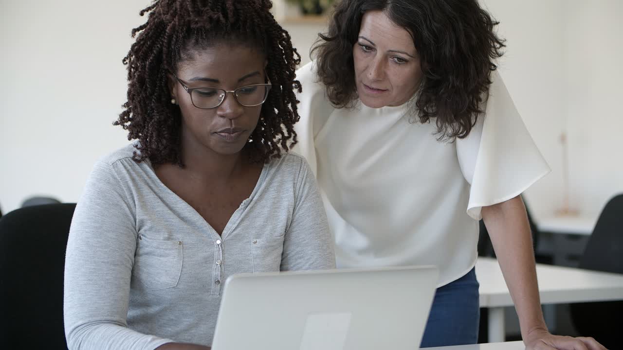 Two confident office workers talking and looking at laptop.