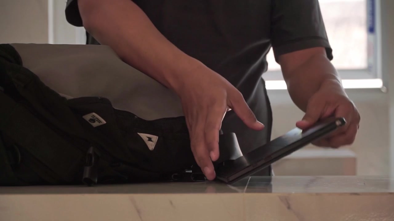 Man packing a tablet and smartphone into a backpack, preparing for travel, work, or study. Modern mobile technology, digital lifestyle, and everyday organization concept.