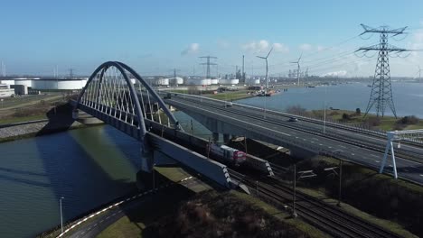 locomotive drives over a railway bridge in an industrial area with petroleum storage tanks