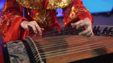 una mujer con un vestido rojo ornamentado toca un instrumento de cuerda tradicional tailandés en bangkok
