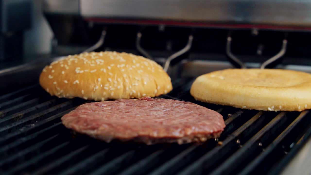 Grilling meat cutlet and burger buns. Frying raw cutlet and bread for hamburger on hot grill with smoke. Junk food preparation