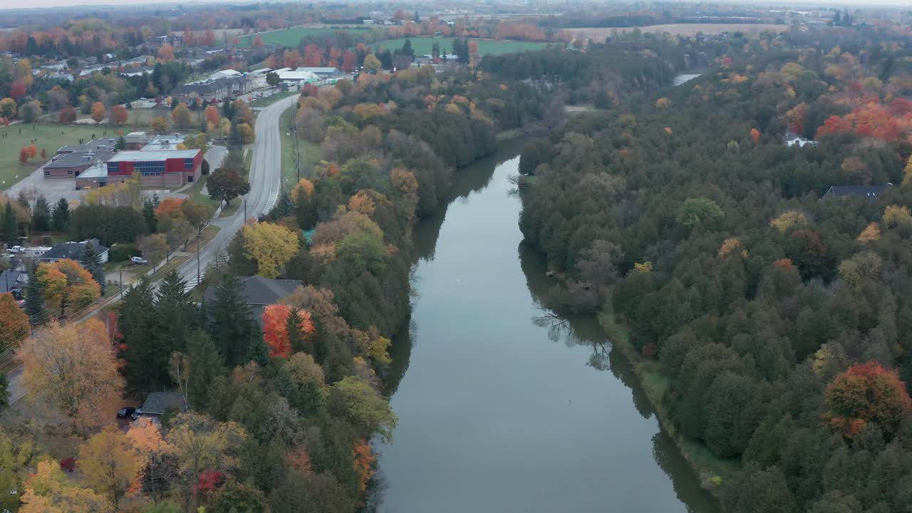 드론 샷은 강의 중간 샷에서 시작하여 뒤로 날아 건물, 자동차 및 쓰러진 나무가 있는 작은 마을을 드러내기 위해 확장됩니다.