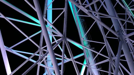 closeup on slowly rotating mechanism of colorful flickering iridescent ferris wheel in amusement park at nighttime