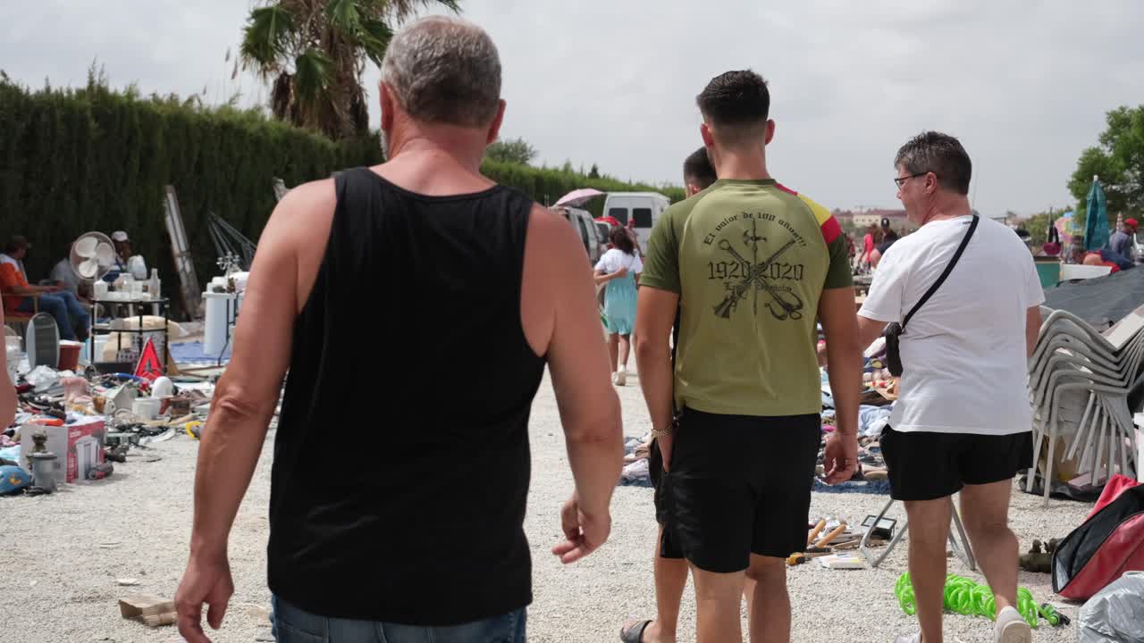 A bustling open-space flea market features a display of household items, including reusable furniture, as shoppers browse and explore the eclectic selection of goods.