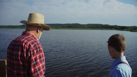 vista trasera de un abuelo con su nieto preparando equipo para pescar juntos