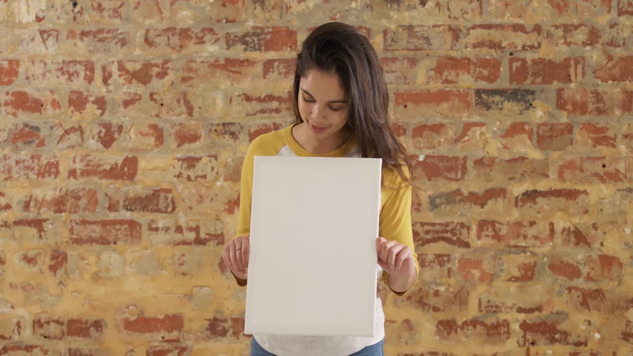 Caucasian woman holding a white rectangle on a brick wall