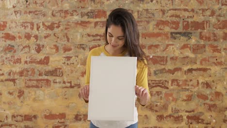 Caucasian-woman-holding-a-white-rectangle-on-a-brick-wall