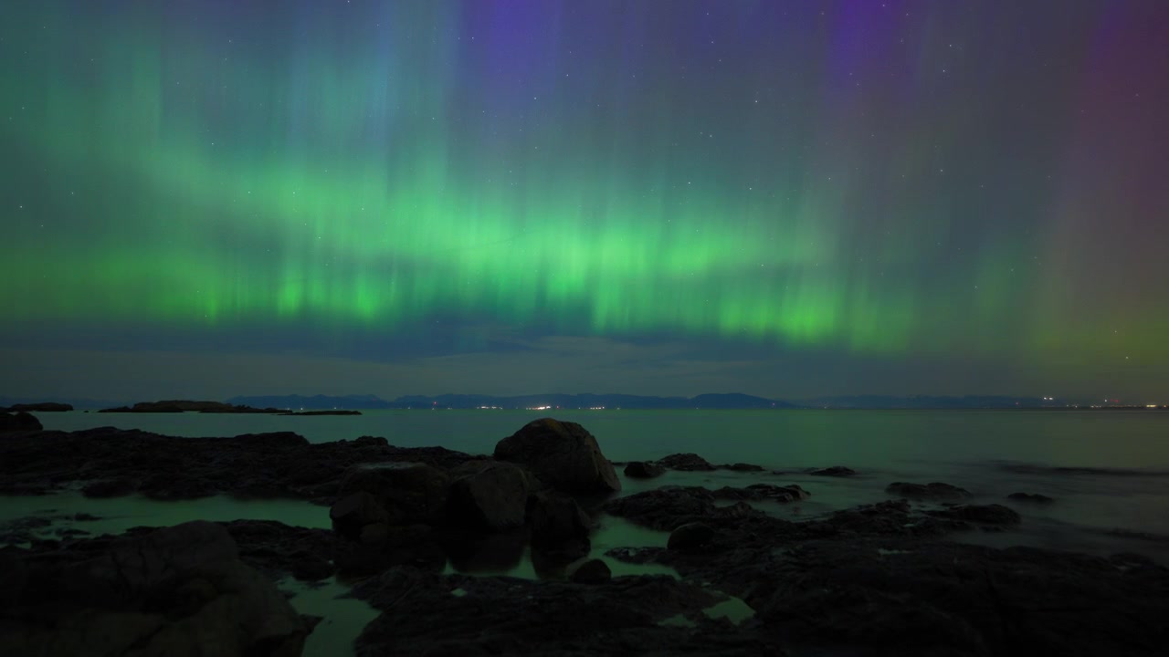 Aurora boreale che brilla di notte e si riflette nell'acqua dell'oceano. Timelapse.