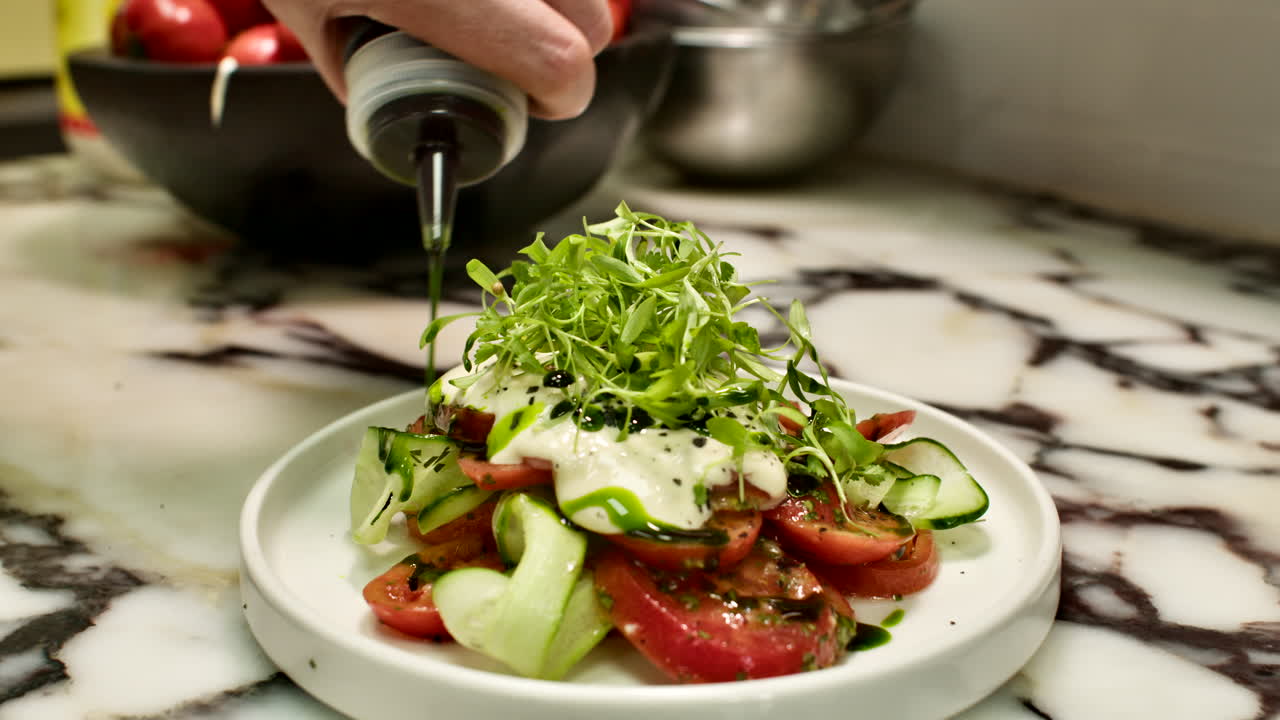 Primo piano di uno chef che irrora glassa balsamica scura su un'insalata fresca di pomodori e cetrioli in un ambiente cucina generico. Presentazione culinaria professionale e food styling salutare.